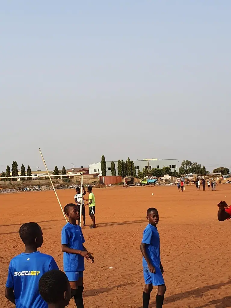 Young players in blue kits gathered on a community football pitch in Ghana