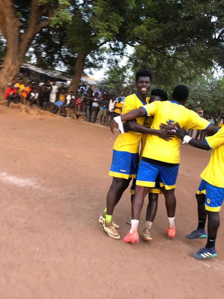 Young players in yellow and blue kits celebrating together on a community football pitch
