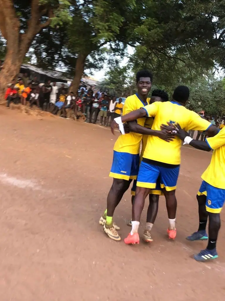 Young players in yellow and blue kits celebrating together on a community football pitch