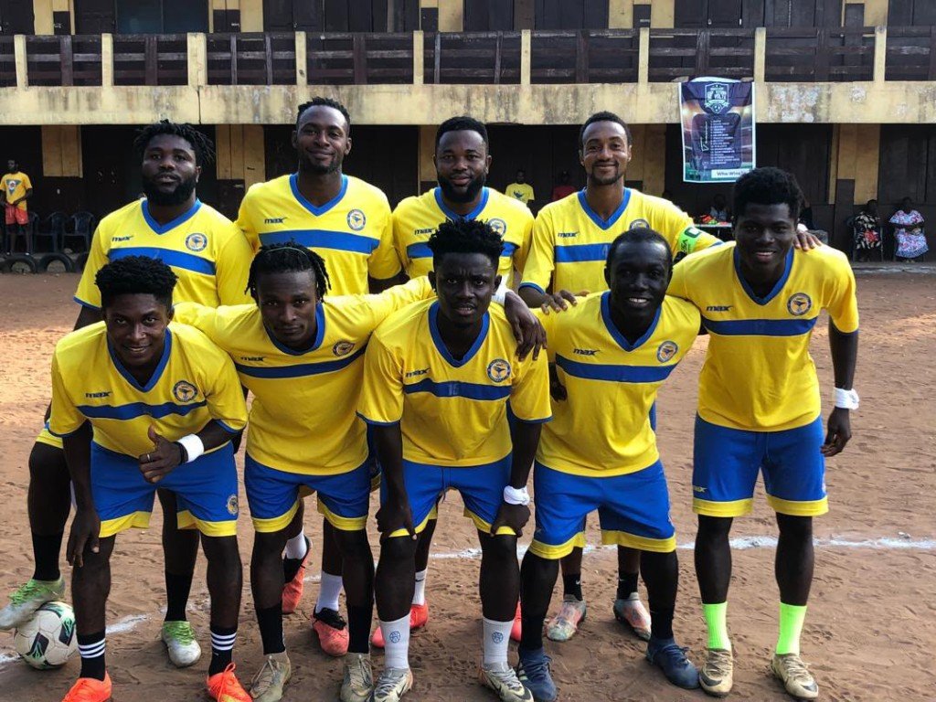 A football team in matching yellow and blue kits gathered together on a community pitch